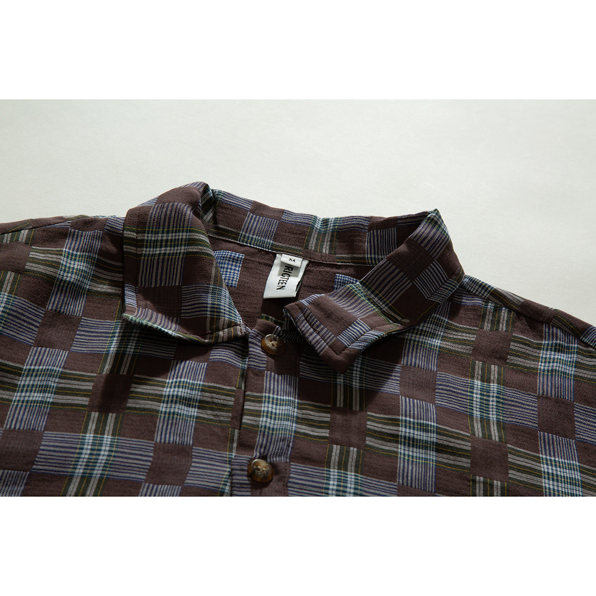 Close view of a brown patchwork-plaid button-up shirt showing its collar, buttons and sewn neck label.