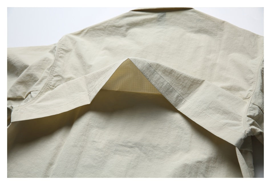 Back view of a light beige shirt jacket with a wide vent-like layered panel across the upper back.