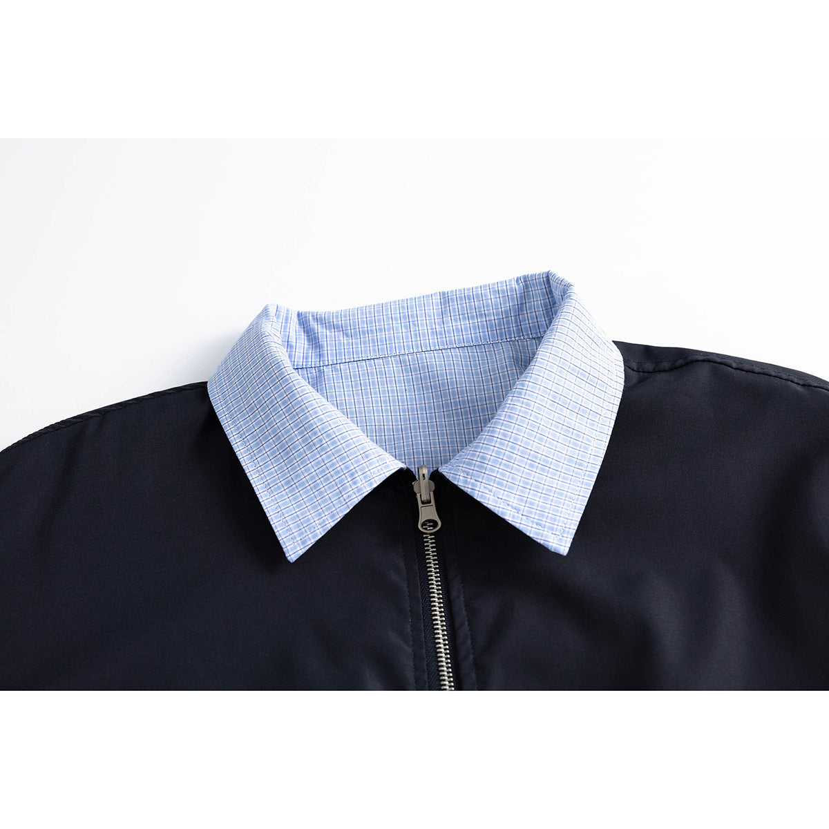 Close-up of a navy jacket with a light blue checked collar and central metal zipper.