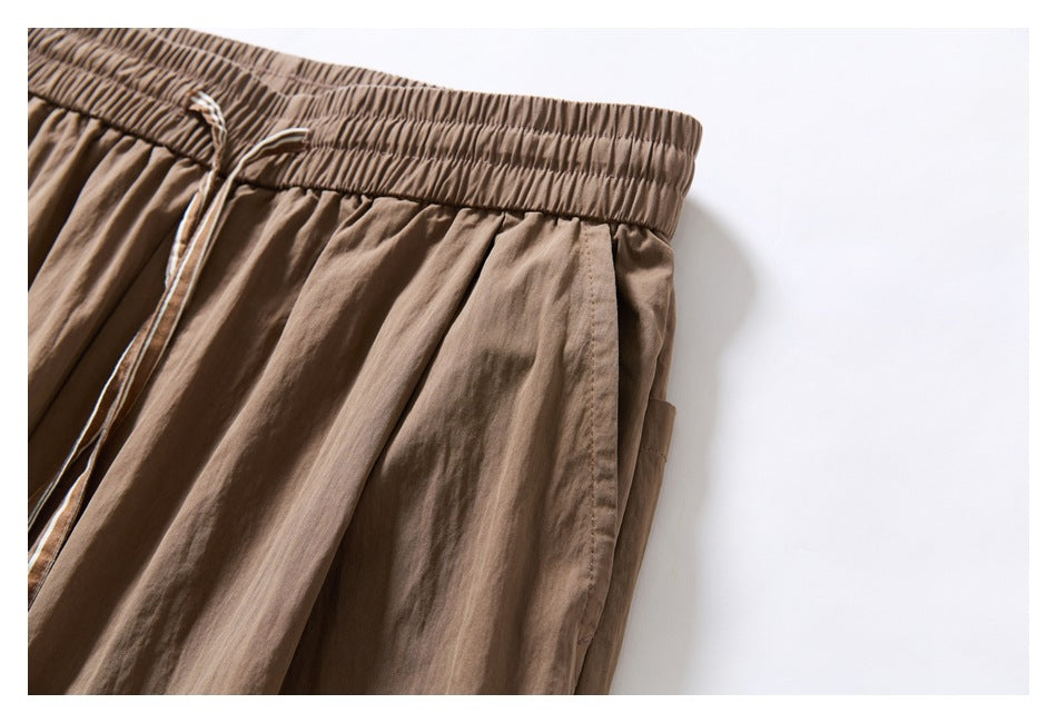 Close-up of taupe trousers showing the elastic waistband, drawstring, and side pocket opening.