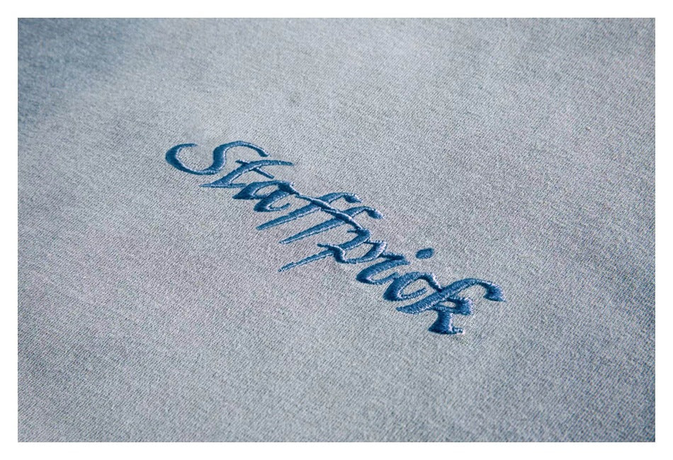 Close-up of blue-gray knit fabric with dark blue cursive embroidery.