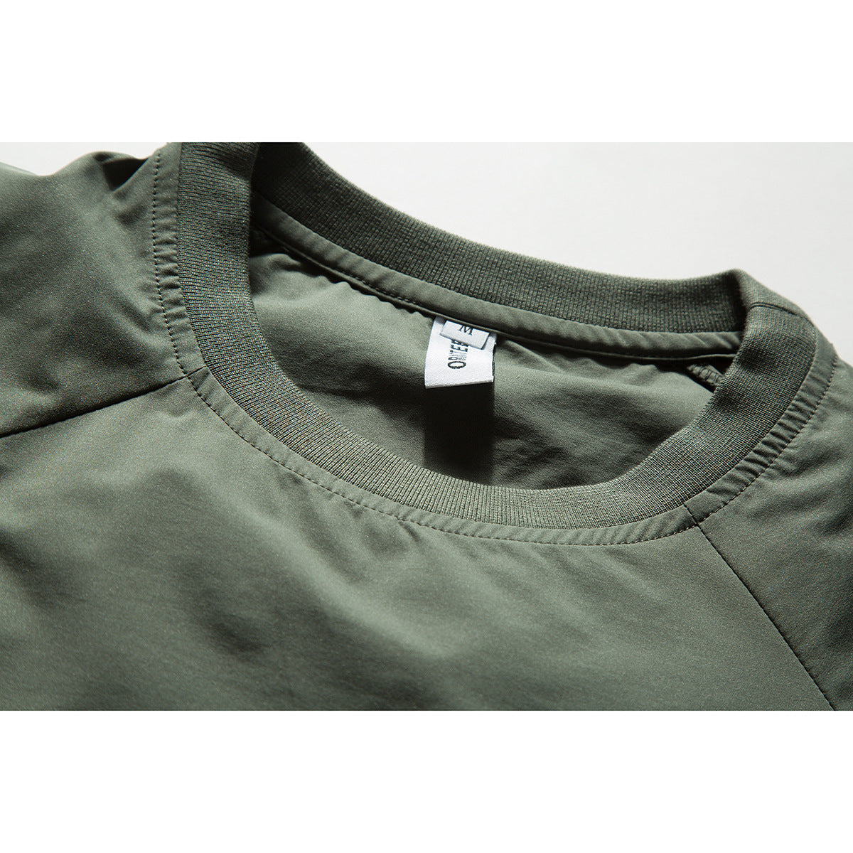 Close-up of an olive-green shirt's ribbed crew neckline and sewn-in neck tag.