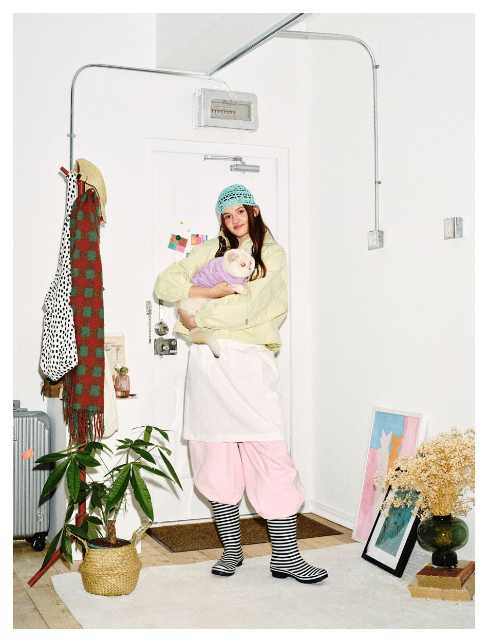 Full-length model wearing a pale yellow cropped jacket and pink trousers while holding a cat.