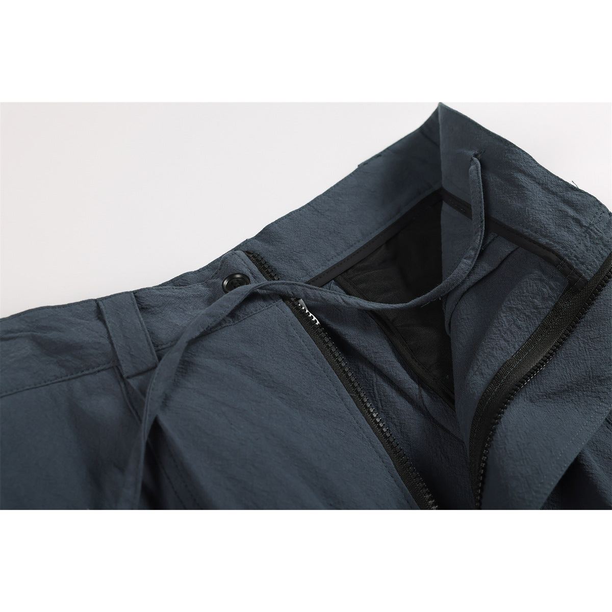 Close-up of dark slate-blue trousers with the waistband open, revealing the zipper and dark inner lining.