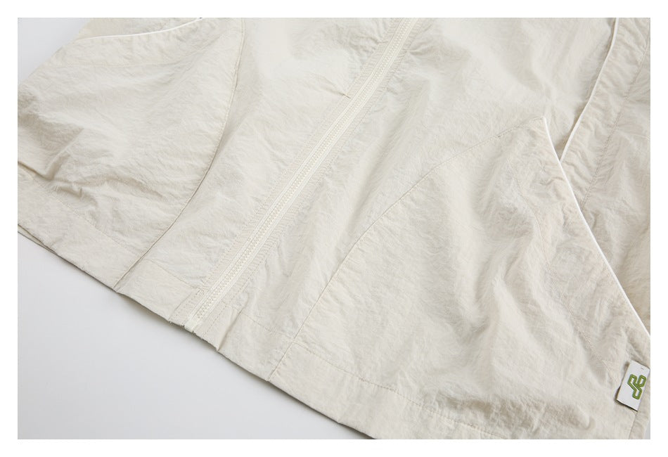 Cream jacket close-up showing a front zipper, seam details, and a small sewn label with a green symbol.