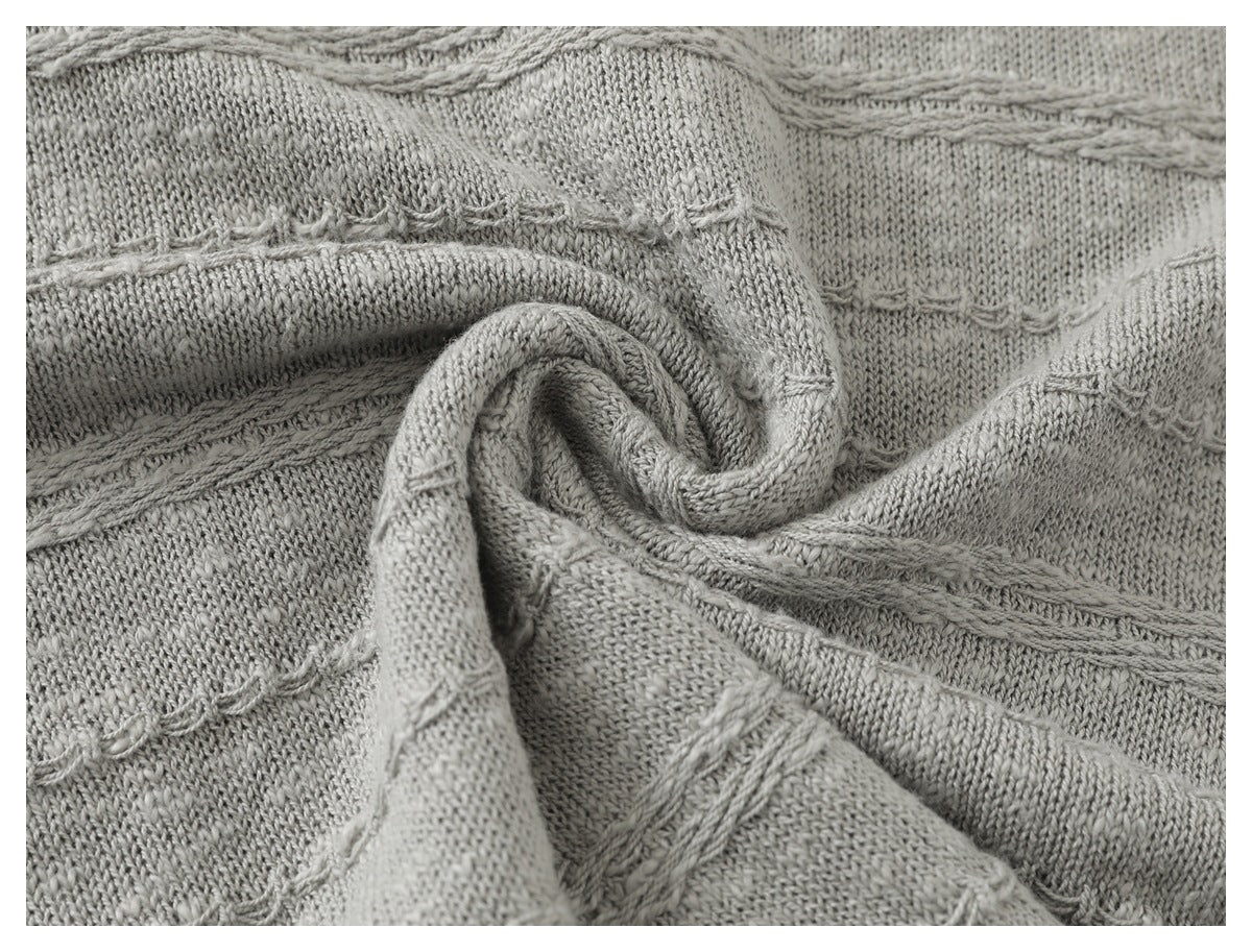Close-up of light gray knit fabric with raised cable-like bands and looped stitch details.