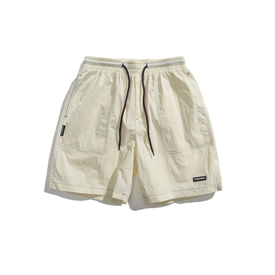 Front view of cream shorts with an elastic waist, long dark drawstrings, large front pockets, and small black patches.