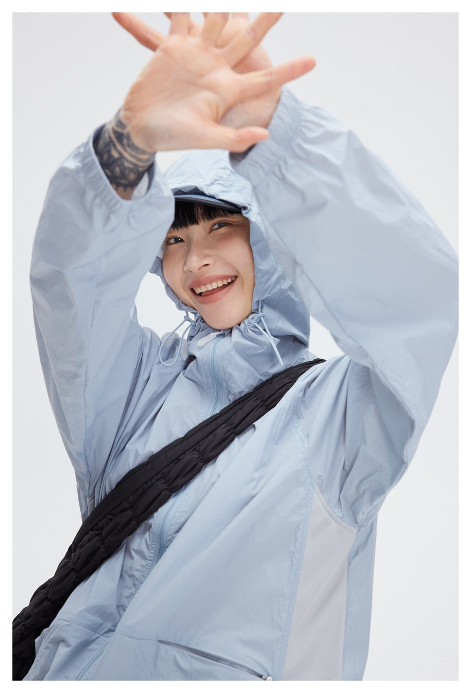 Close view of a pale blue jacket’s raised hood, drawcords, zip front, and light mesh side panel on a model.