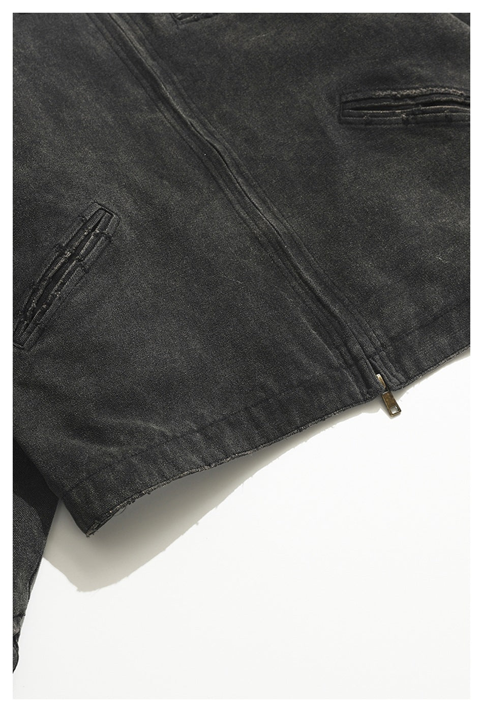 Close-up of a charcoal jacket's front pockets, stitching, and lower zipper.