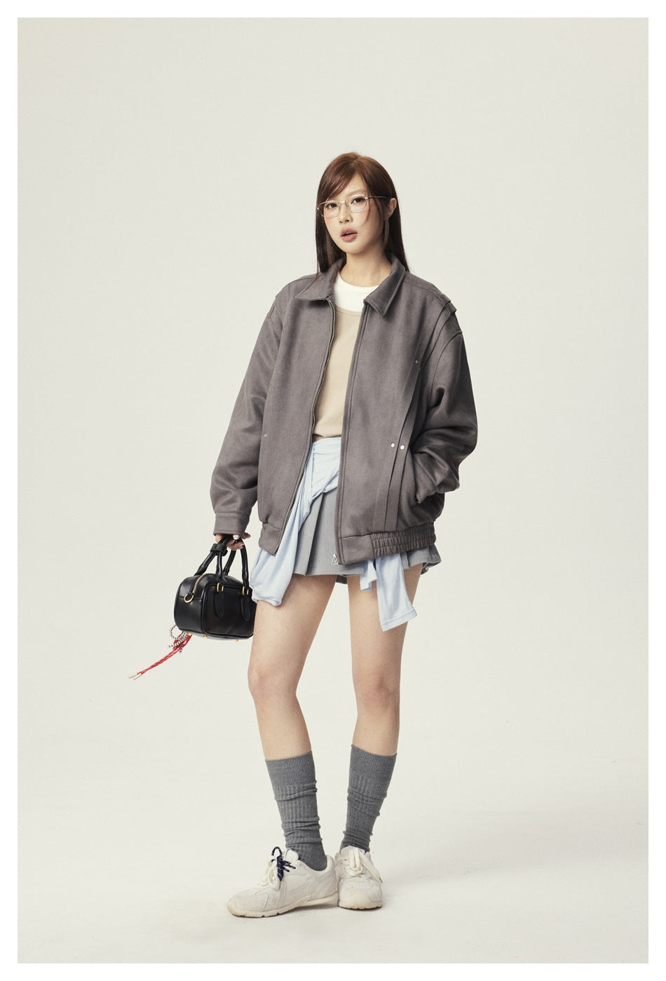 Full-length model in an oversized gray zip jacket, layered top, short gray skirt, and sneakers.