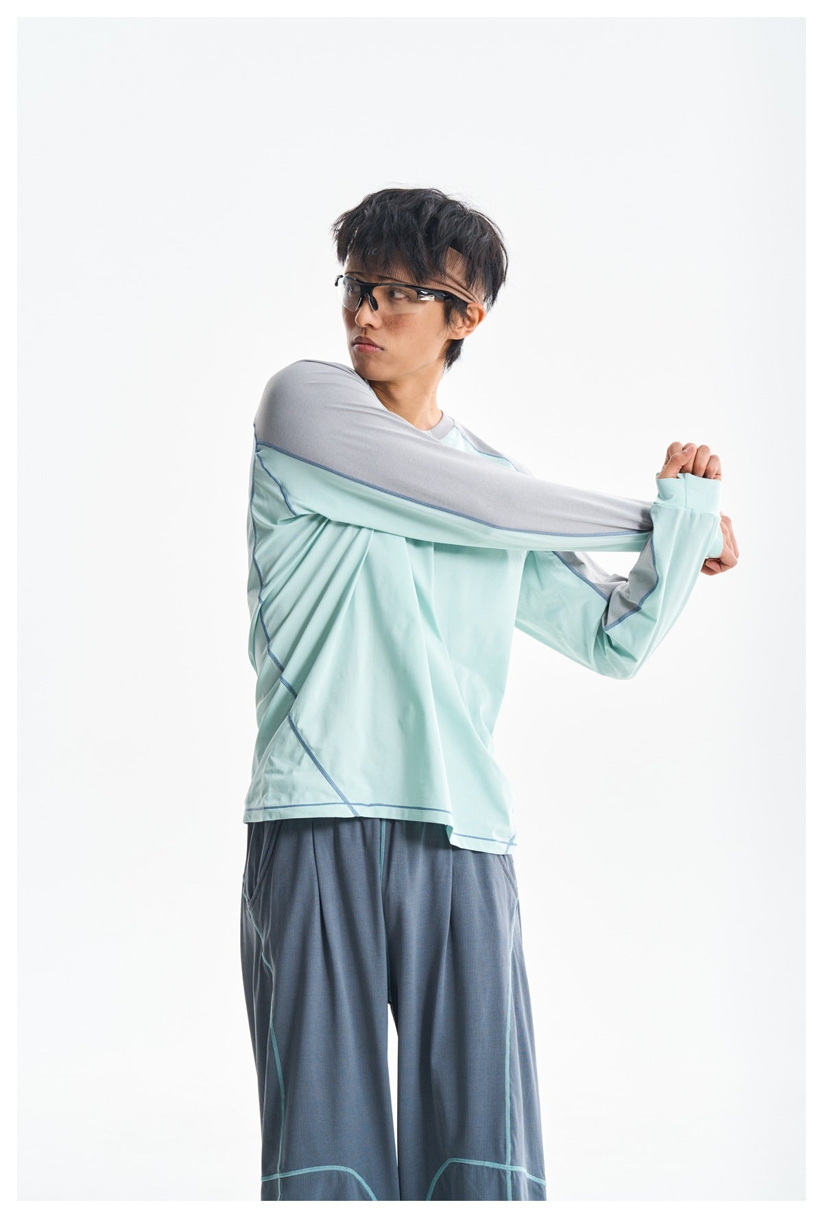 Model stretches one sleeve of a mint-green and gray color-block long-sleeve shirt with slate-blue trousers.