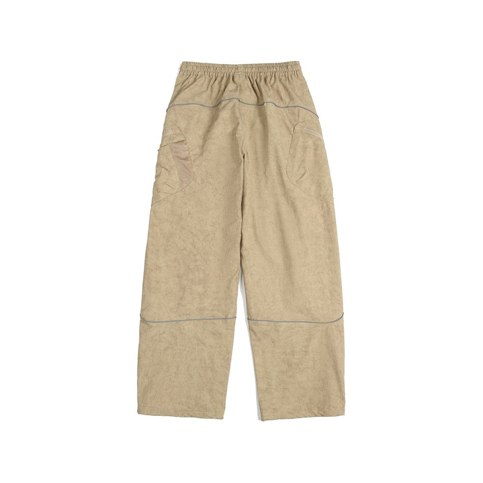 Back view of loose tan pants with an elastic waist, curved gray piping, and large side pockets.