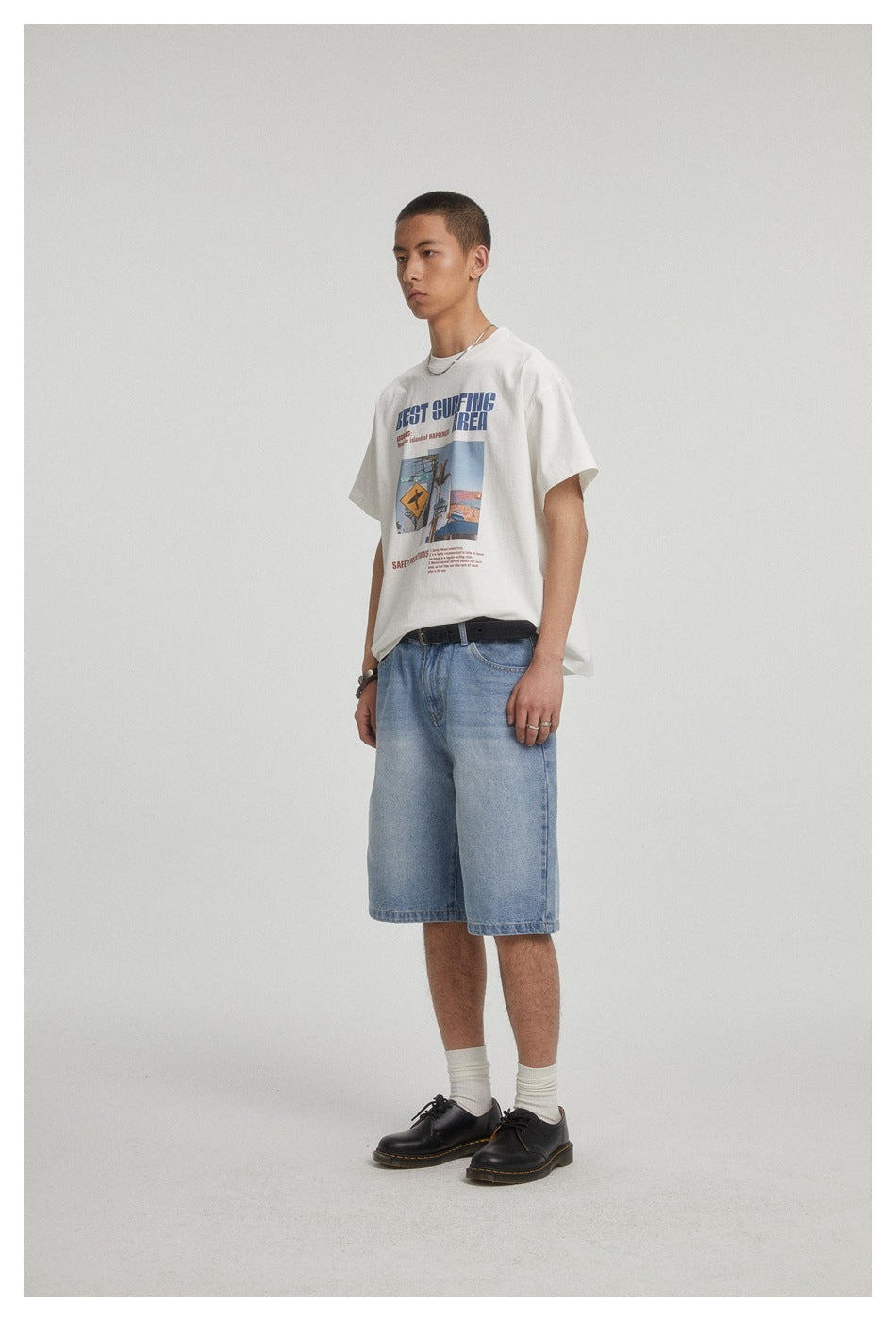 Three-quarter view of a model wearing a white graphic T-shirt and light blue denim shorts.