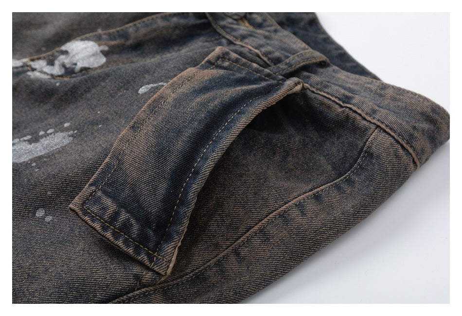 Close-up of a dark washed denim pocket and seam with light paint-splatter marks.