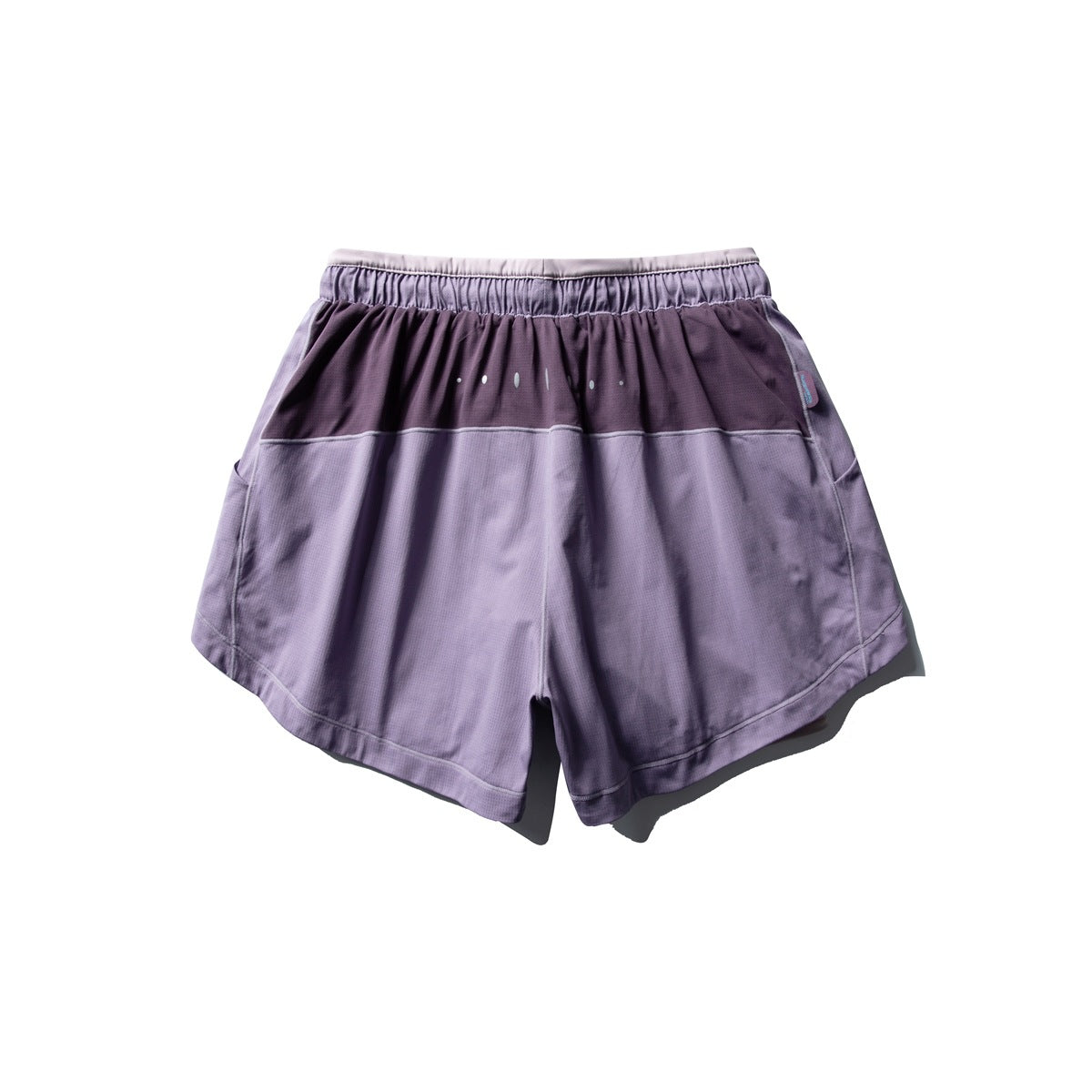 Back view of purple running shorts with a dark upper panel, elastic waistband, small dot accents and curved hems.