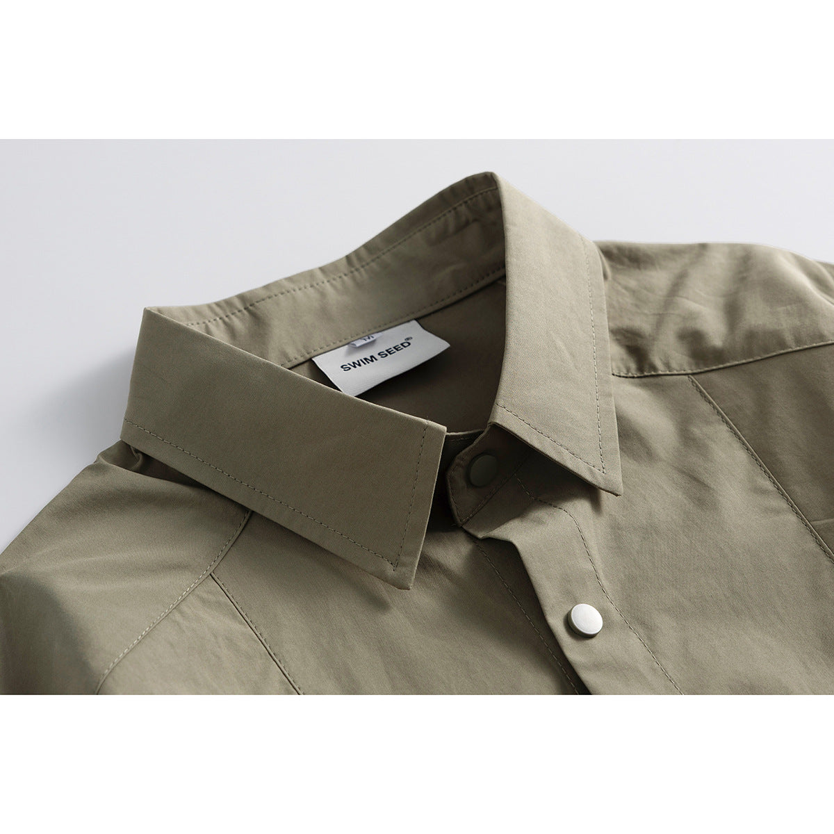 Close-up of an olive-khaki shirt collar, stitched seams, snap buttons and inner label.