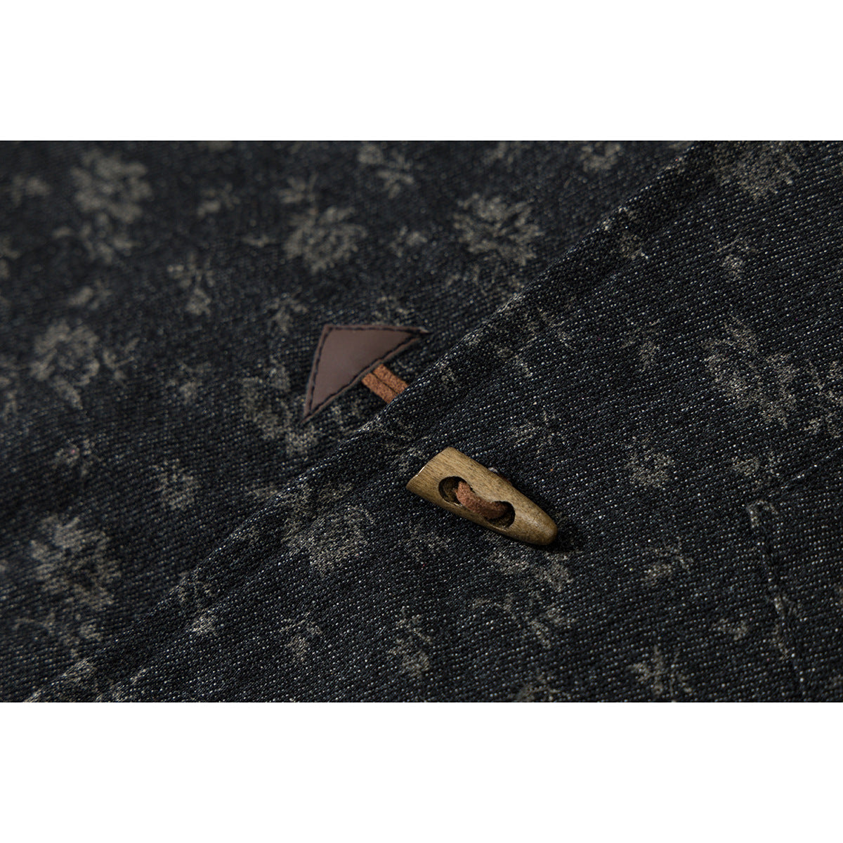 Close-up of dark floral-patterned fabric with a wooden toggle button and small triangular accent.