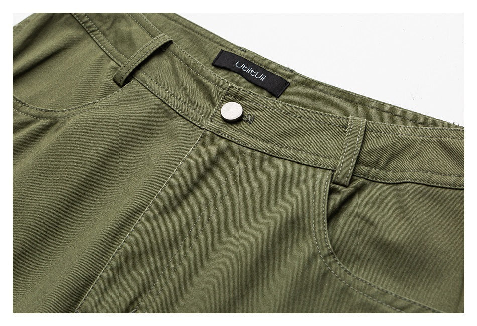 Close-up of olive-green trousers showing the waistband, silver button, belt loops, front pocket seam, and sewn-in label.