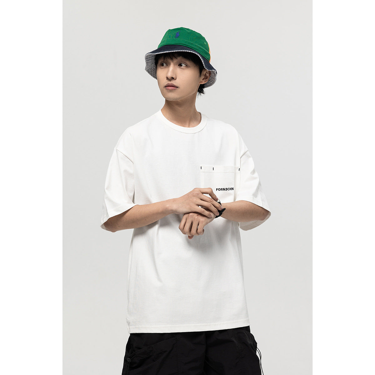Model wearing a white oversized T-shirt with a large stitched chest pocket and black text.