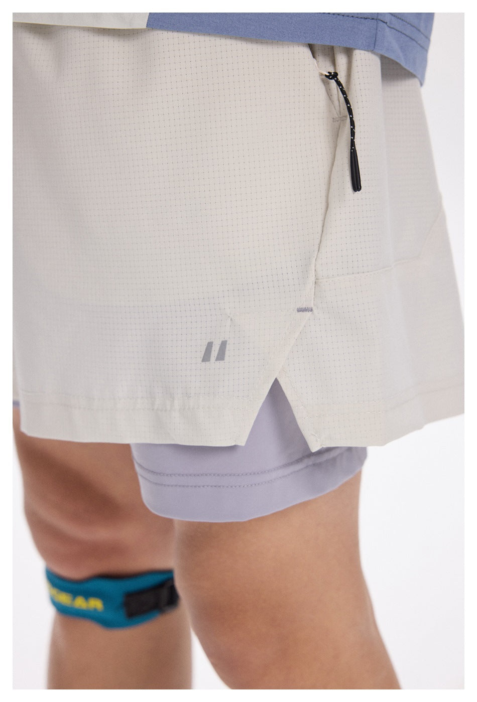 Close-up of light gray shorts showing the dotted texture, black drawcord, split hem, and layered lavender shorts underneath.