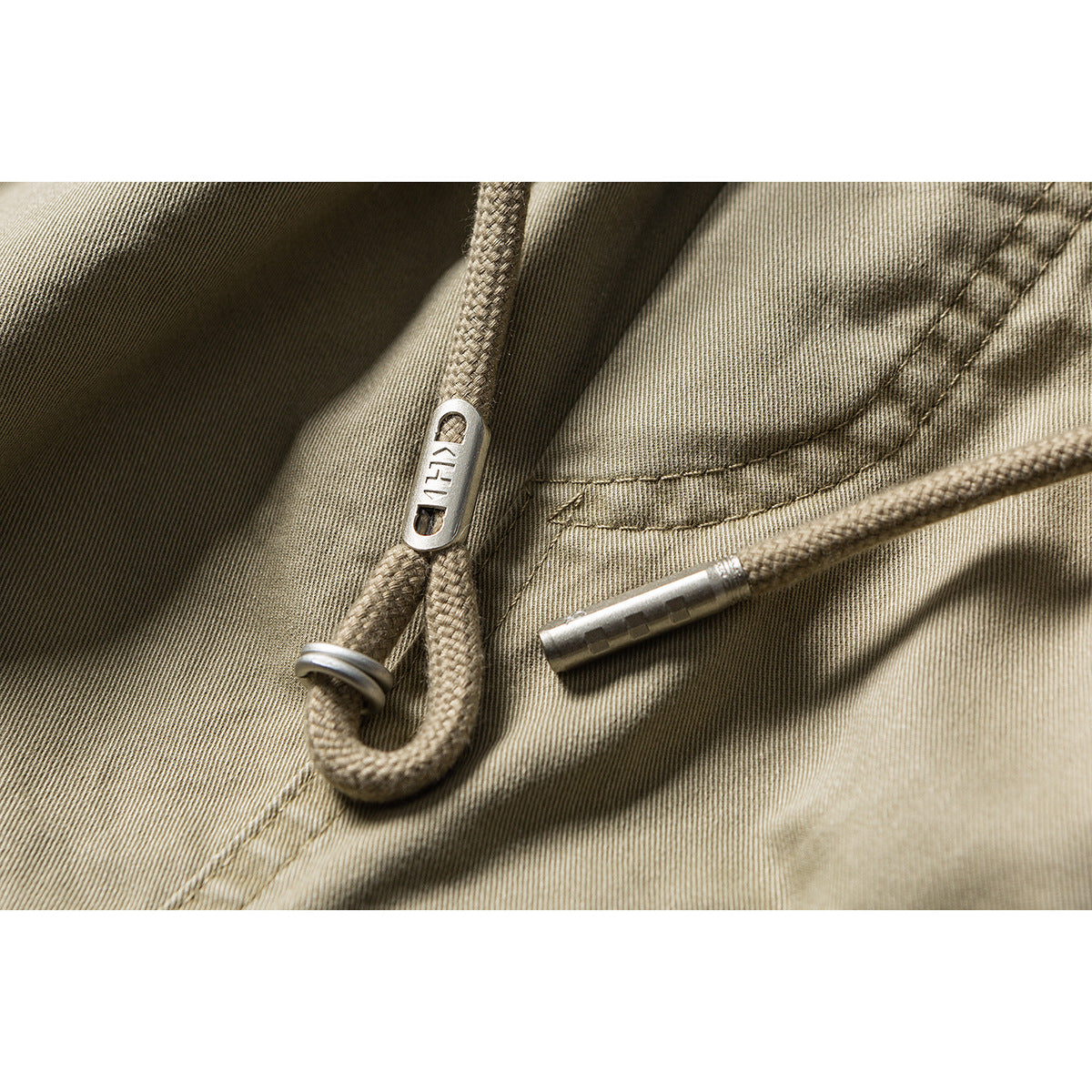 Close-up of khaki shorts fabric and braided drawstring with metal ends, one stamped with lettering.