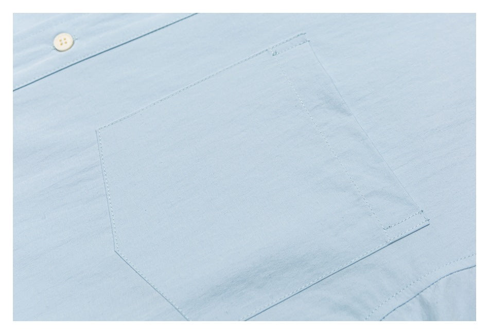 Close-up of the light blue shirt's single chest pocket and stitching.