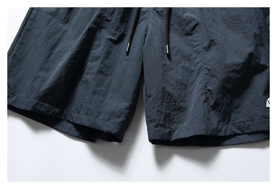Close-up of navy shorts showing the lower hems, drawcord ends, seams, and perforated panels.