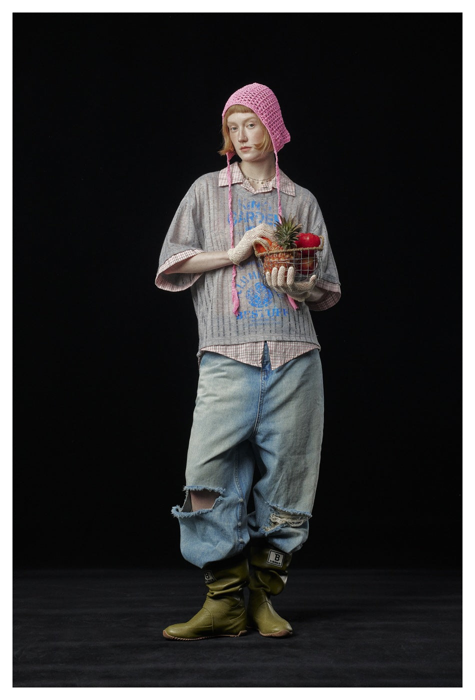 Model wearing a gray striped blue-graphic top over a checked shirt, pink crocheted bonnet and loose distressed jeans.