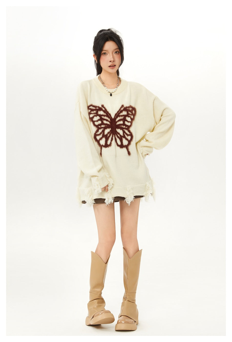 Model wearing an ivory oversized sweater with a large fuzzy brown butterfly and distressed fringe along the cuffs and hem.