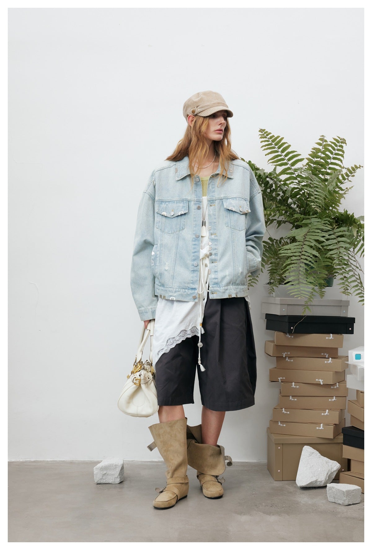 Model wearing a light-wash denim jacket over a white lace-trimmed top and black shorts, with tan boots.