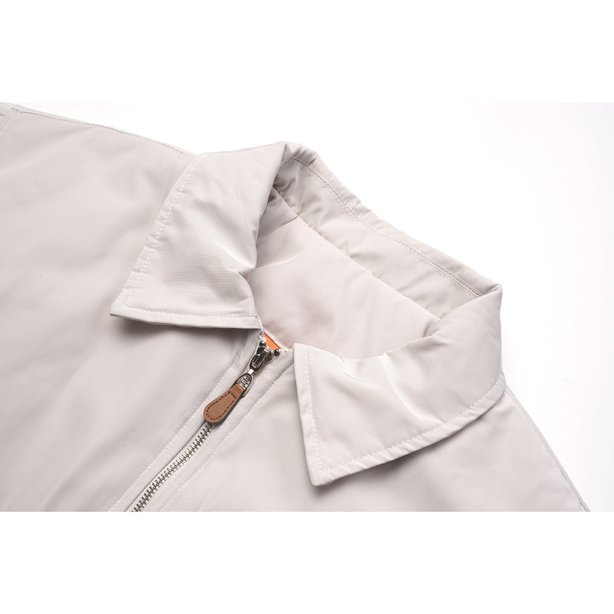 Close-up of a pale gray jacket's pointed collar and silver front zipper with a brown pull.