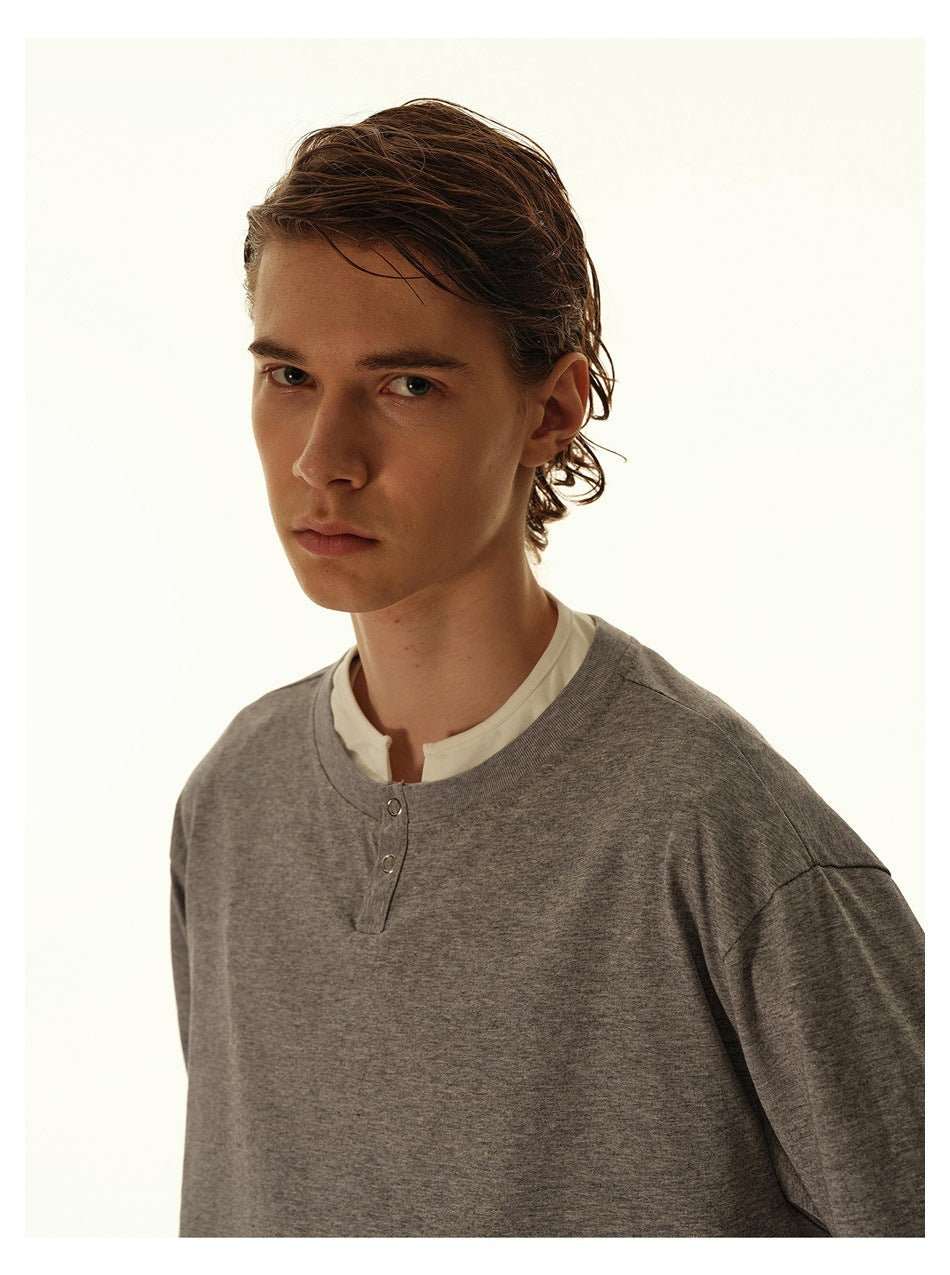 Model wearing a heather gray long-sleeve henley-style top over a white shirt, shown from the chest up.