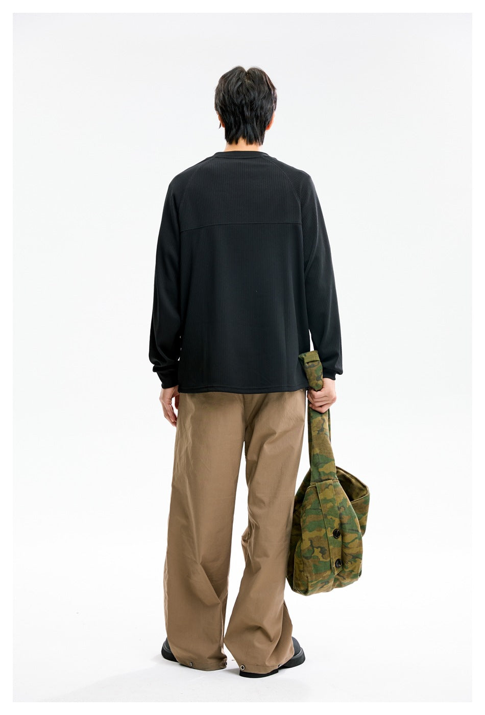 Back view of a model wearing a black long-sleeve ribbed top with a horizontal upper-back seam and loose tan pants.