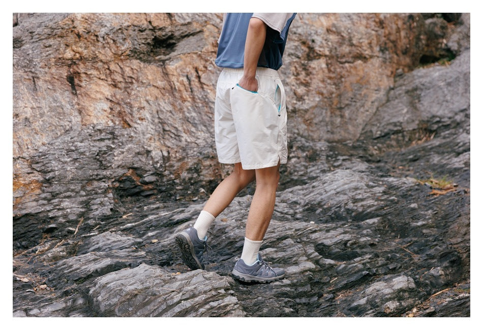 Hiker wearing off-white shorts with turquoise pocket trim, seen from the side while walking over rocky terrain.