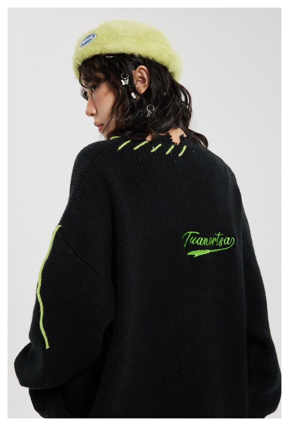 Rear close-up of a model wearing a black knit sweater with green stitching and green script embroidery