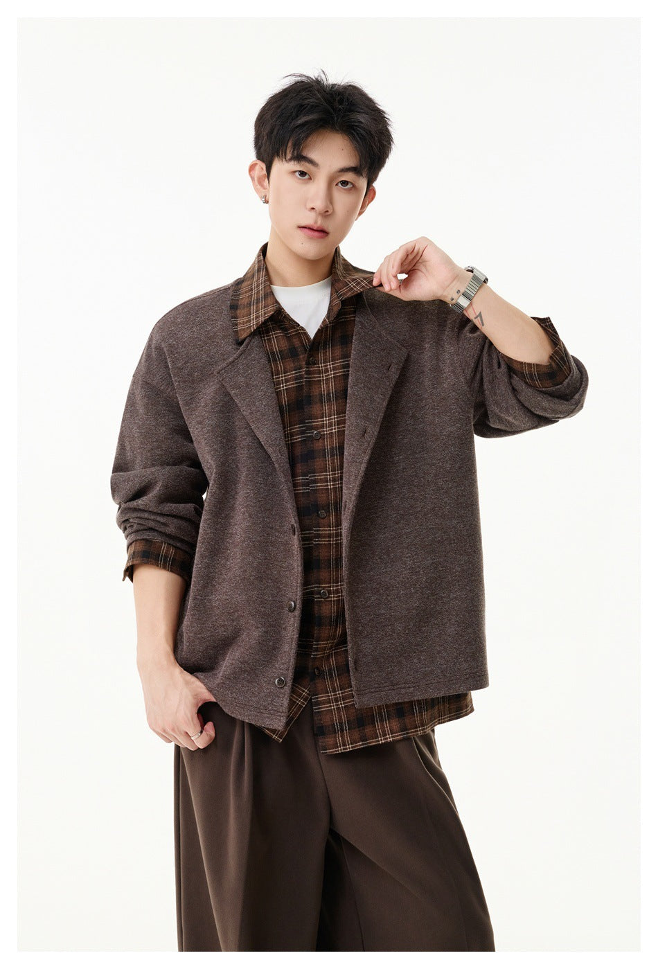 Model wears a loose brown jacket over a brown plaid shirt, with sleeves pushed up to show the plaid cuffs.