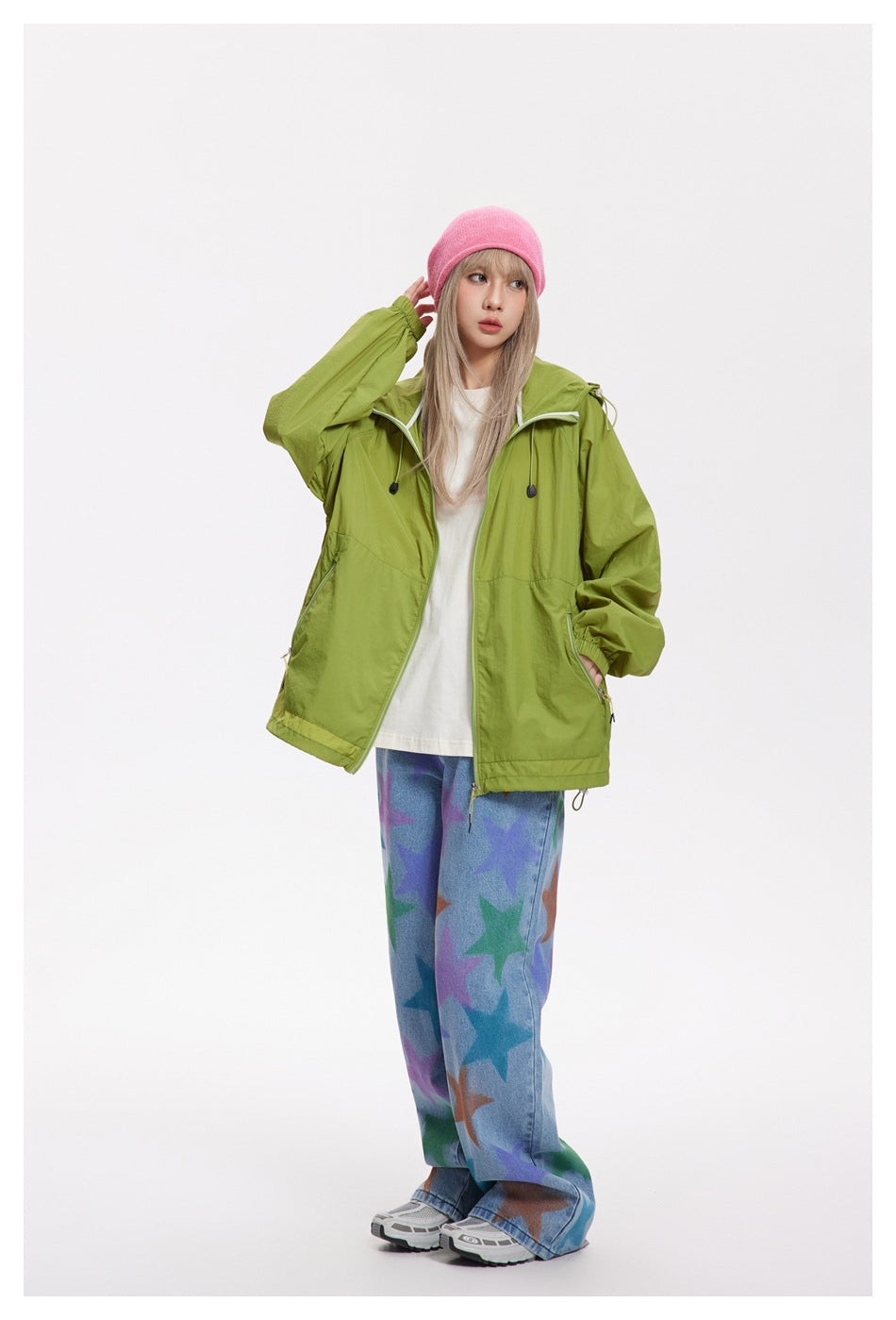 Model in green hooded zip jacket over a white tee with star-print jeans, hand raised, three-quarter view