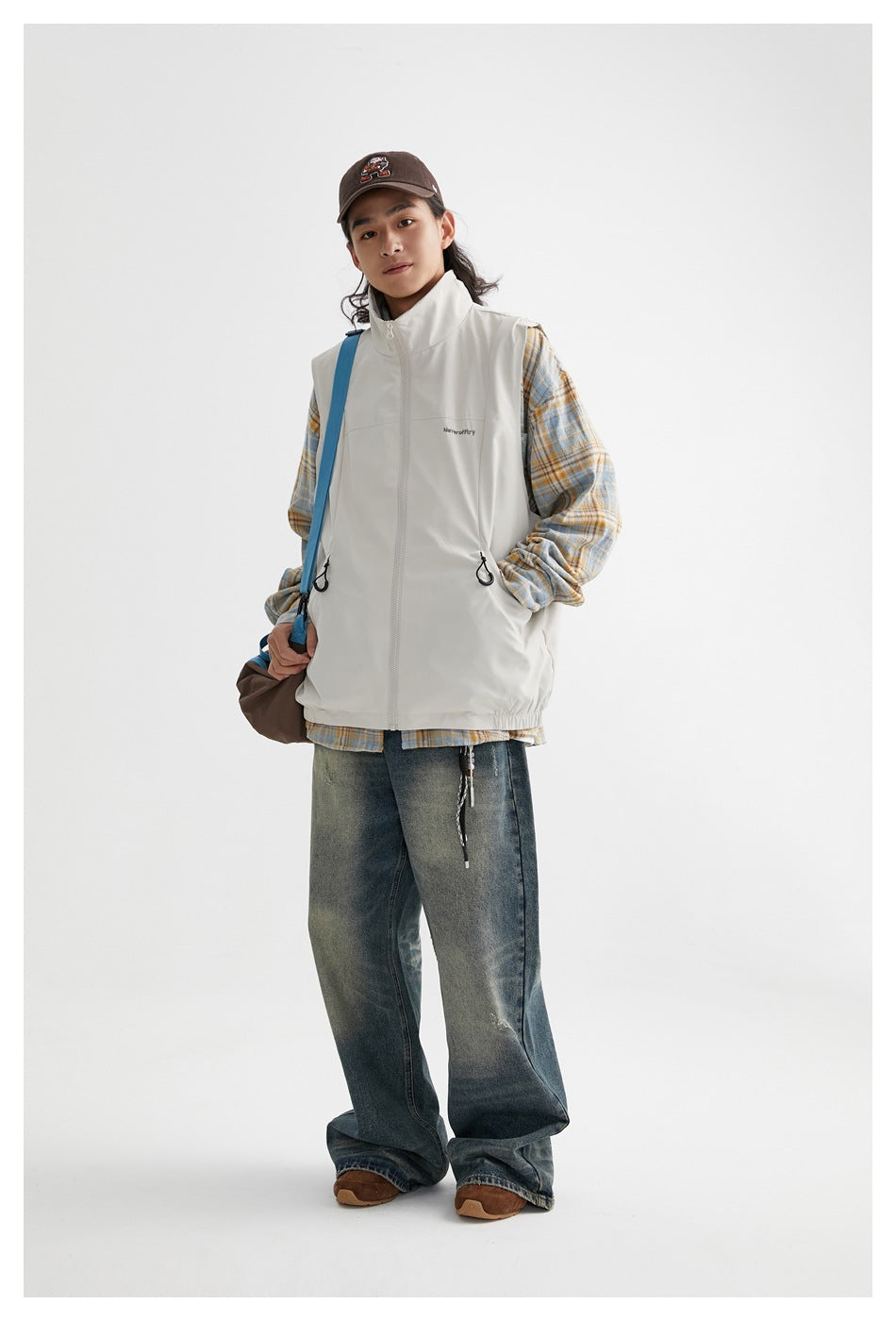 Full-length front view of a model wearing an off-white sleeveless zip vest over a blue and ochre plaid shirt.