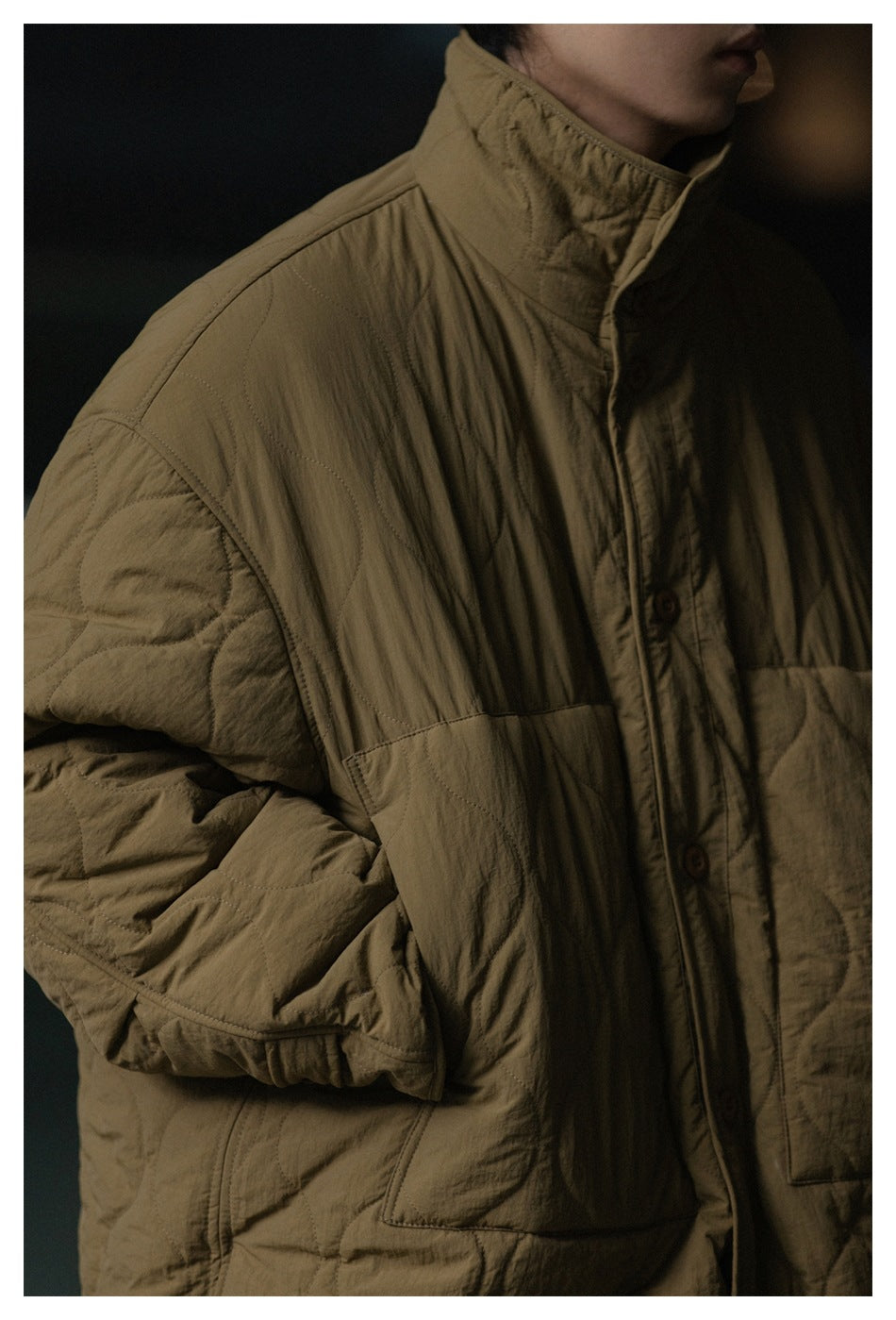 Close-up of an olive-brown quilted coat showing its high collar, button placket, stitching, and sleeve construction.