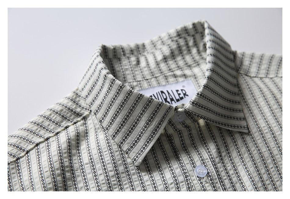 Close-up of the pointed collar, top buttons and sewn neck label on the cream patterned shirt.