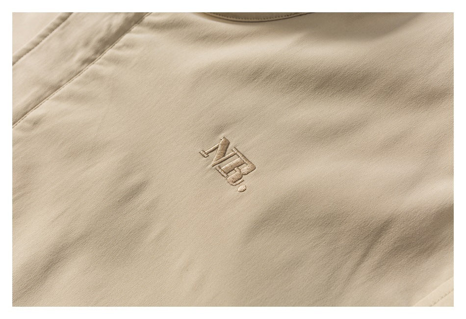 Close-up of a small tonal embroidered emblem on tan jacket fabric.