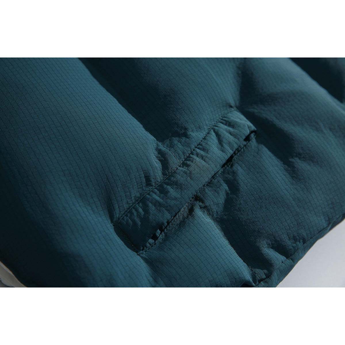 Close-up of dark teal grid-textured padding and a stitched seam on the vest.