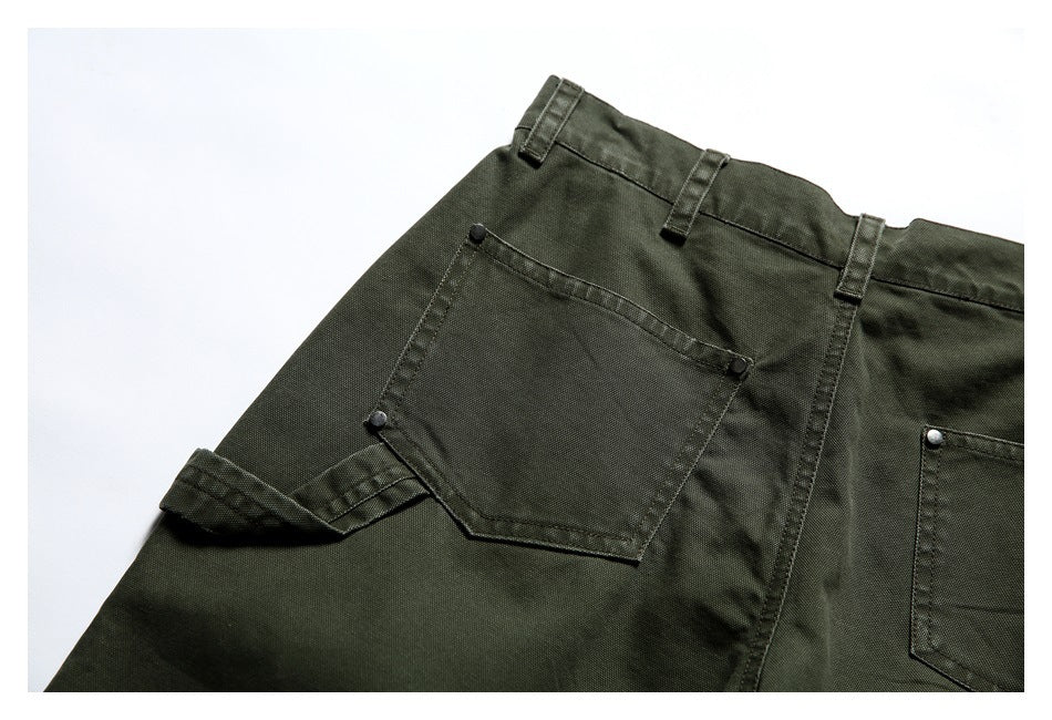 Close-up of olive trousers with belt loops, patch pockets and metal rivets.