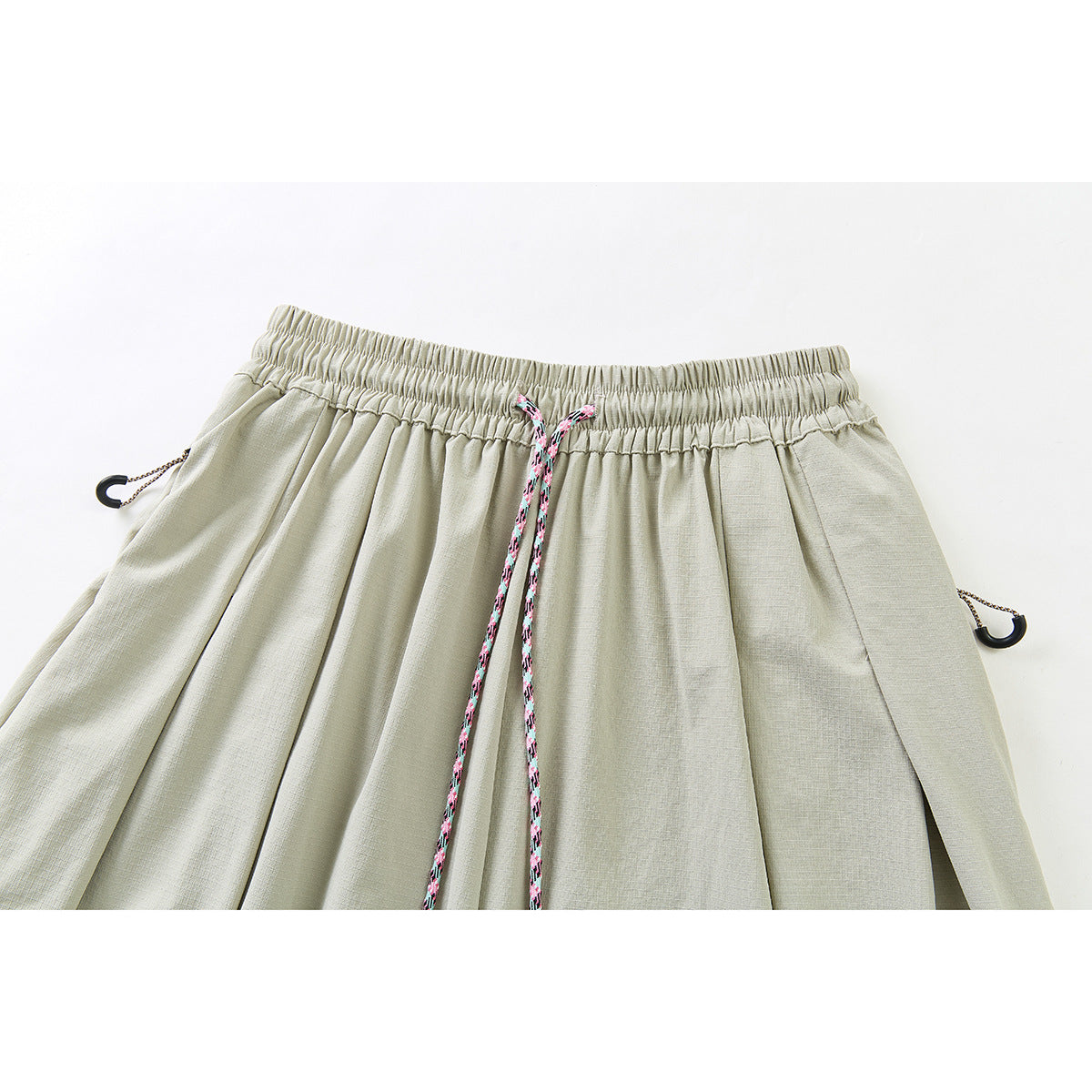 Close-up of pale sage wide-leg pants with an elastic waistband, pink patterned drawstring, and side cord toggles.