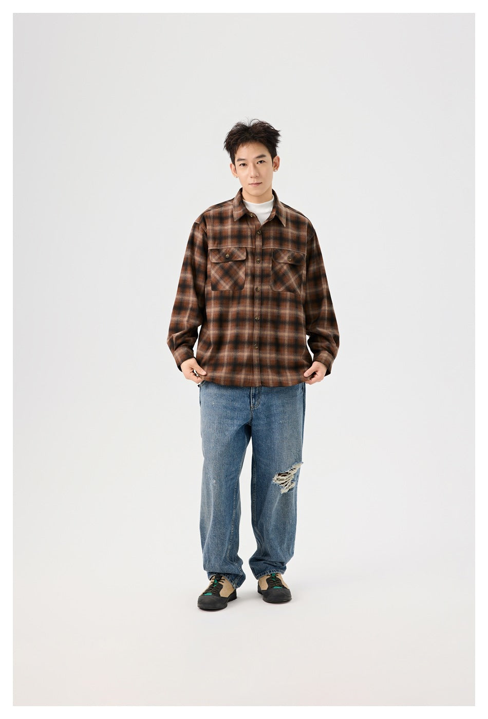 Model wearing a brown plaid button-up overshirt with two flap chest pockets, white top, loose blue jeans, and sneakers.