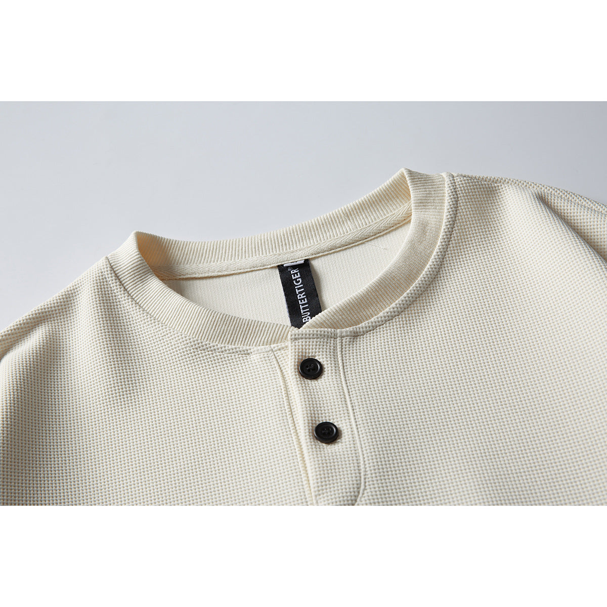Close-up of an ivory waffle-knit sweatshirt neckline and two-button placket with a black neck label.