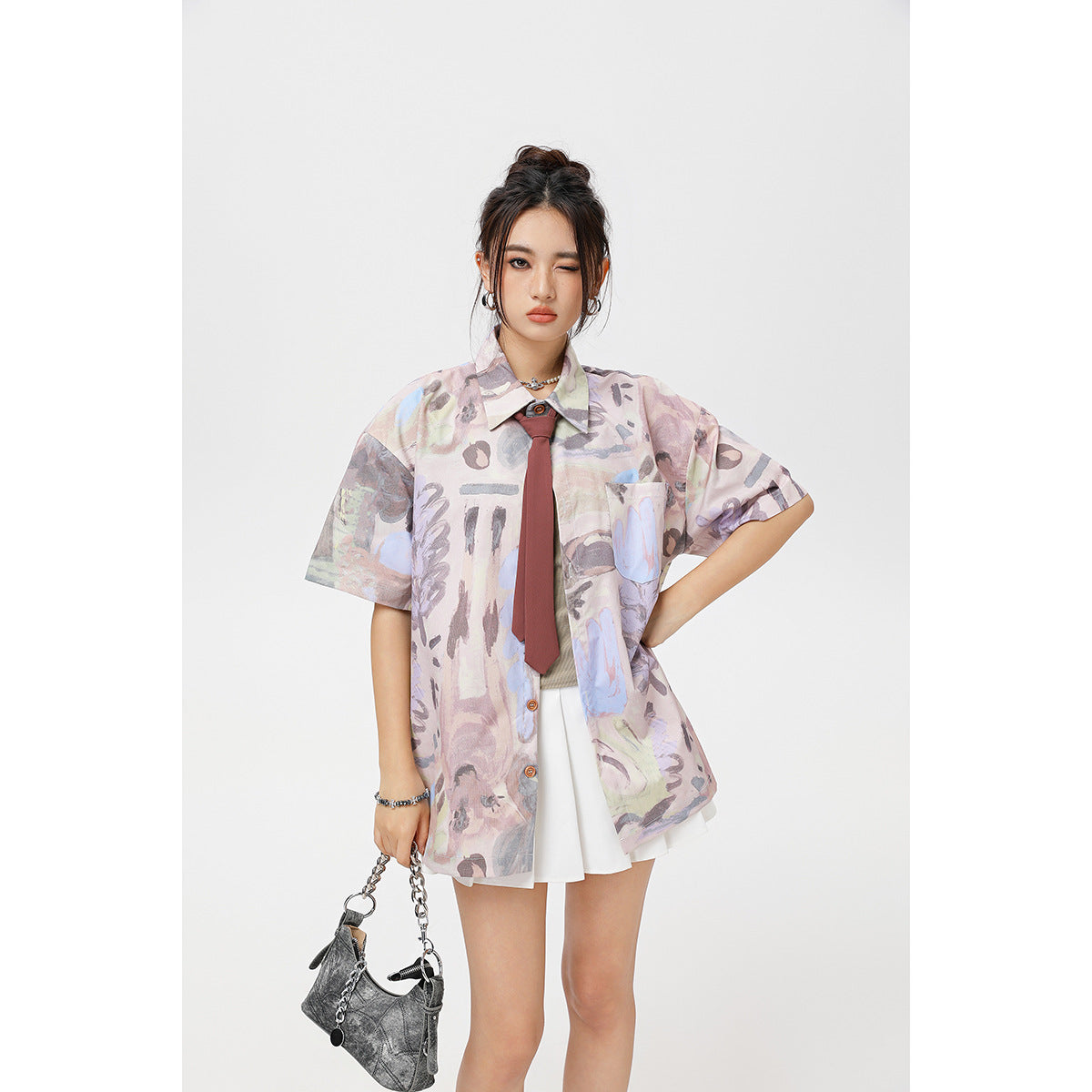 Model wearing a pastel abstract-print oversized short-sleeve shirt with a chest pocket, burgundy tie and white skirt.
