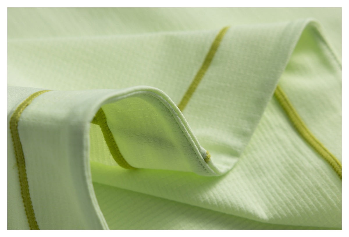 Close-up of pale lime garment fabric and curved seam finishes with yellow-green stitching.