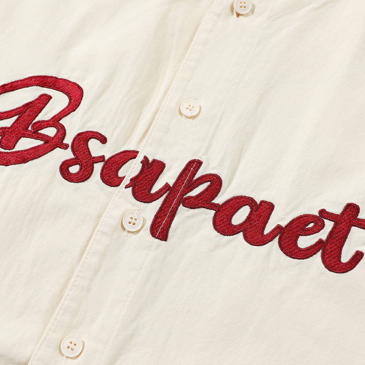 Close-up of an ivory button-front shirt with red embroidered script across the chest.