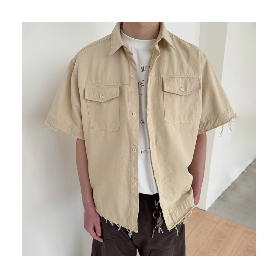 Person wearing the light khaki short-sleeve work shirt open over a white graphic tee, with frayed hem and flap pockets